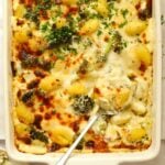 An oven dish filled with baked cheesy gnocchi with broccoli, and a spoon ready to serve up.