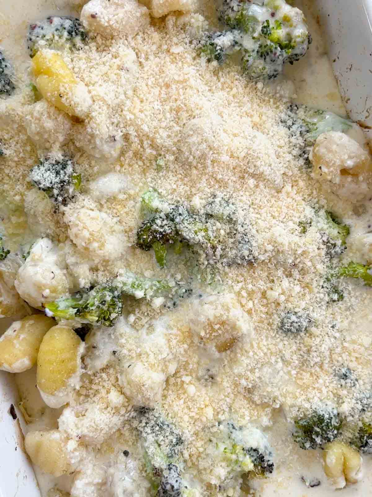 An oven dish with broccoli, gnocchi and parmesan over the top, uncooked.