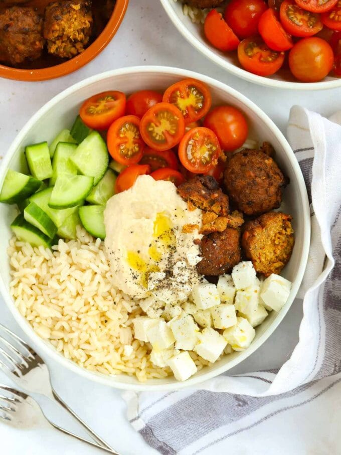 A bowl filled with falafel, tomatoes, cucumber, rice, feta and hummus.
