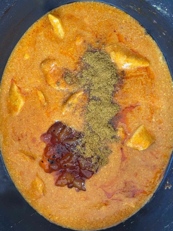 A curry cooking in a slow cooker pan with spices and mango chutney on top, yet to be stirred in.