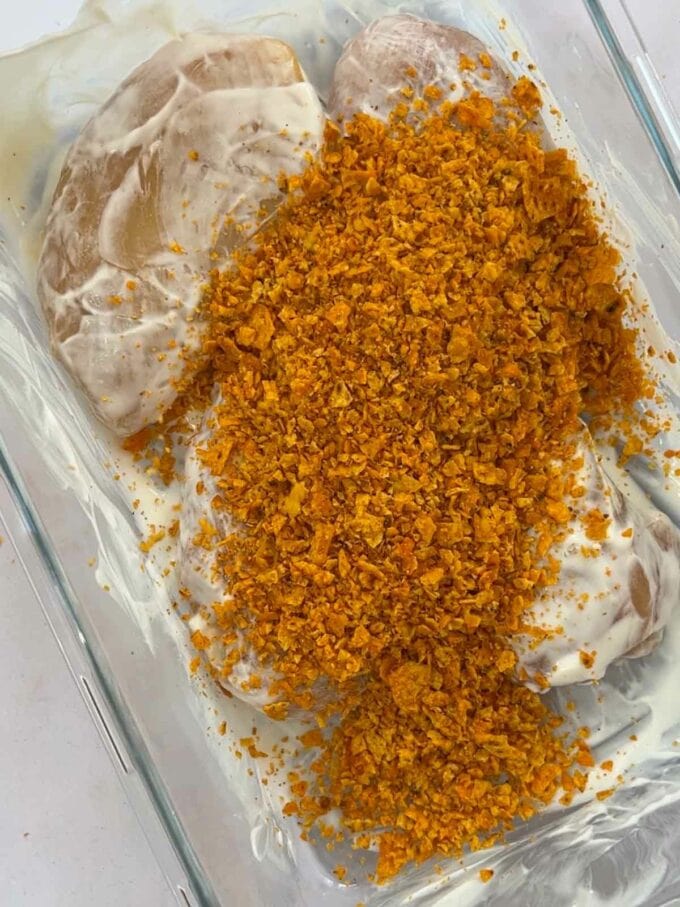 Chicken breasts in a container, coated with yoghurt and tortilla chips.