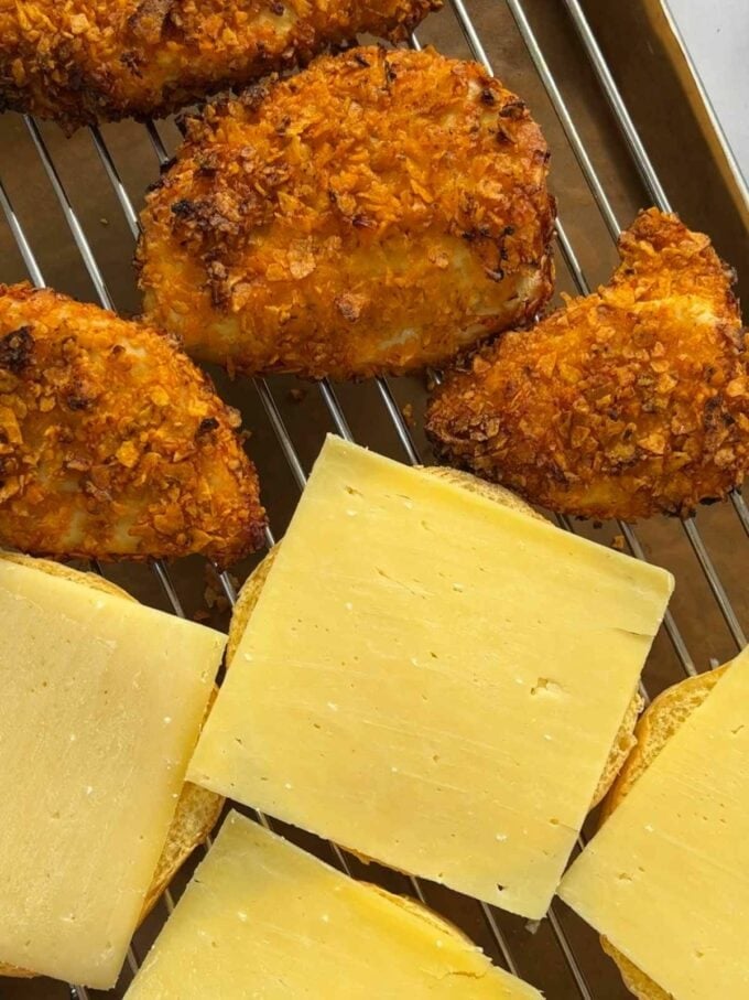 Crispy chicken breast burgers on a grill with slices of cheese.