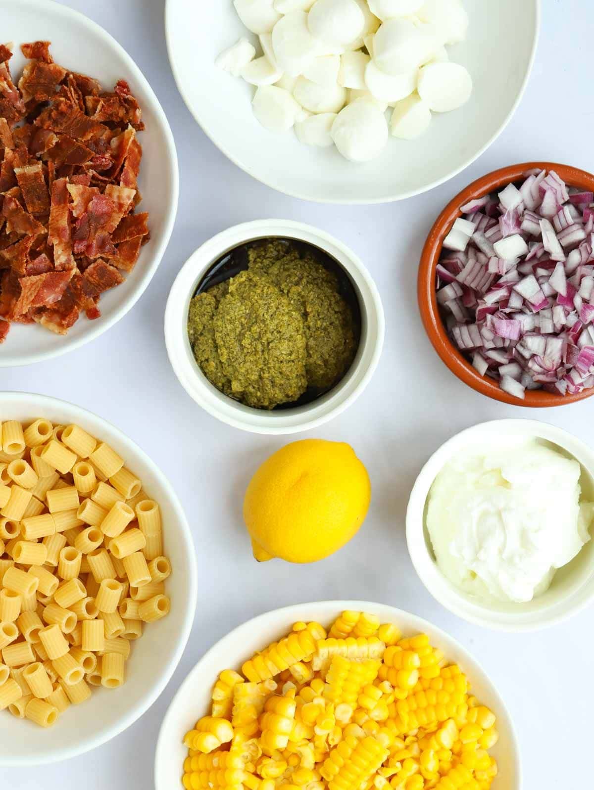 Ingredients for a pesto pasta salad recipe laid on a white counter top.