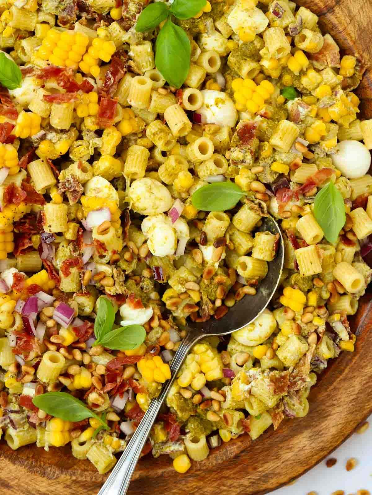 A big bowl full of Pesto Pasta Salad, with a spoon about to serve.