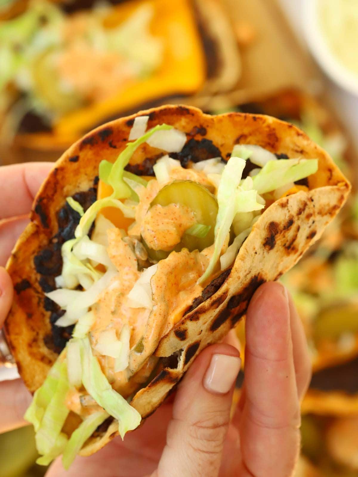 A hand holding a big mac taco, filled with cheese, salad and sauce on top.