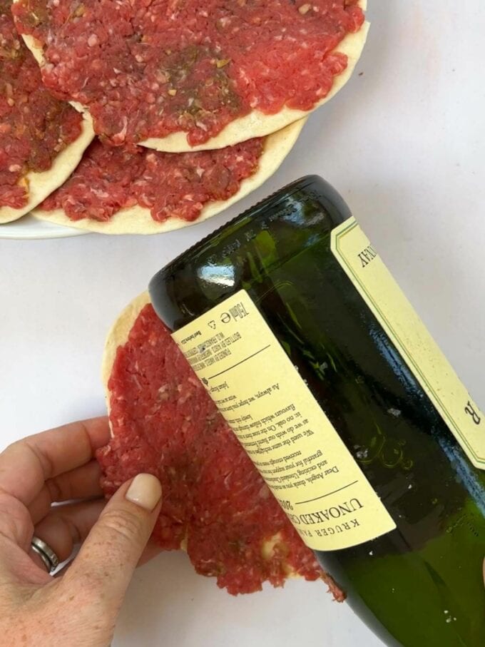 Rolling beef patties onto a tortilla wrap with a wine bottle to flatten it.