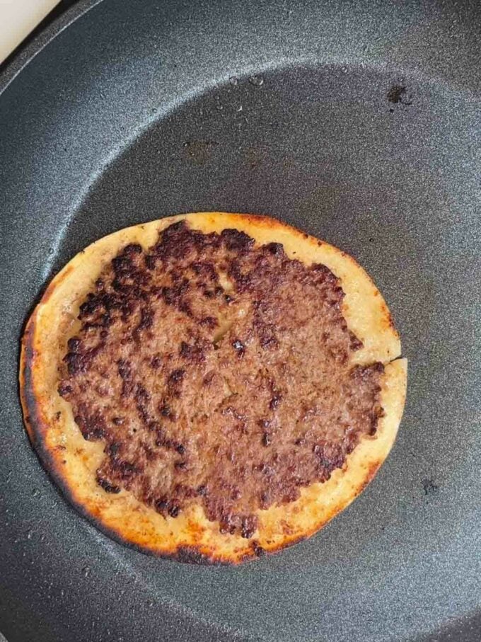 Beef patties on tortilla wrap being fried in a pan.