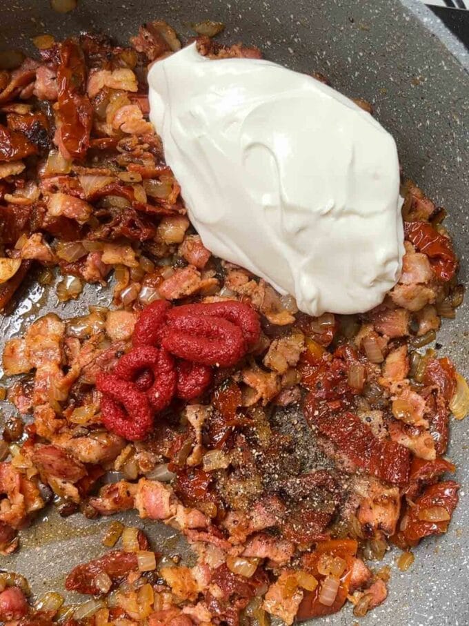 A dollop of cream cheese added to a pan of fried sundried tomatoes, onion and bacon for the recipe Bacon Pasta. Step 3.