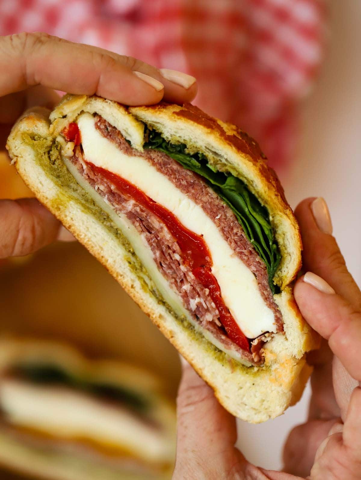Two hands holding a stuffed Muffaletta picnic loaf, about to take a bite.