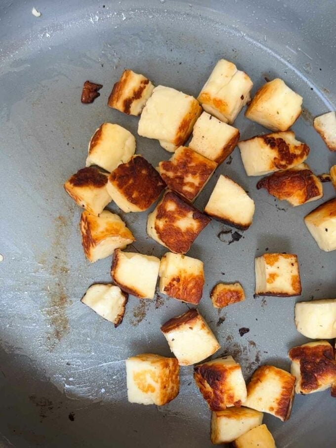 Cubes of halloumi being fried in a pan.