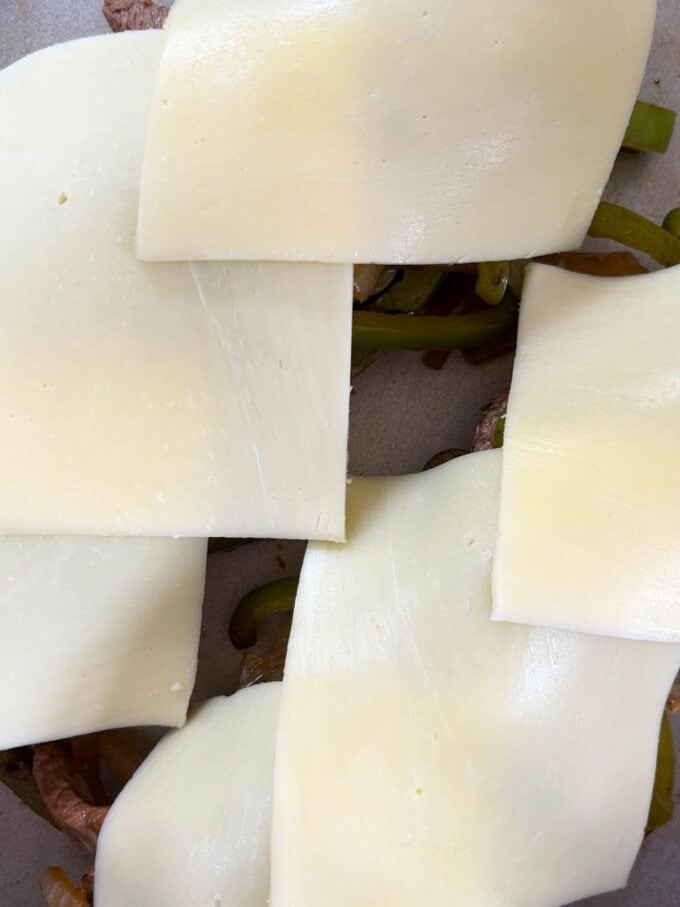 Mozzarella slices on top of steak and vegetables for step 4 in the recipe for Philly Cheesesteak.