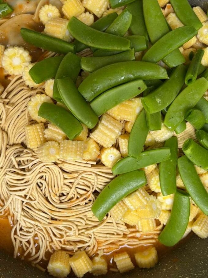 Uncooked vegetables and noodles in a pan for step 4 in the recipe for Gyoza Soup.