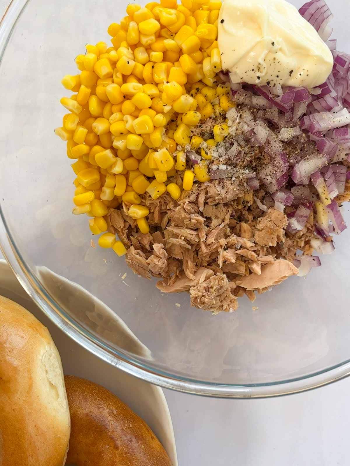 Step 1 of making tuna melt bagels. All the ingredients in a glass bowl, ready to be mixed.