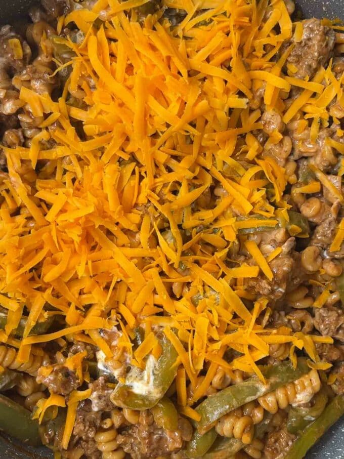 Cheese on top a pan of cooking mince and pasta.