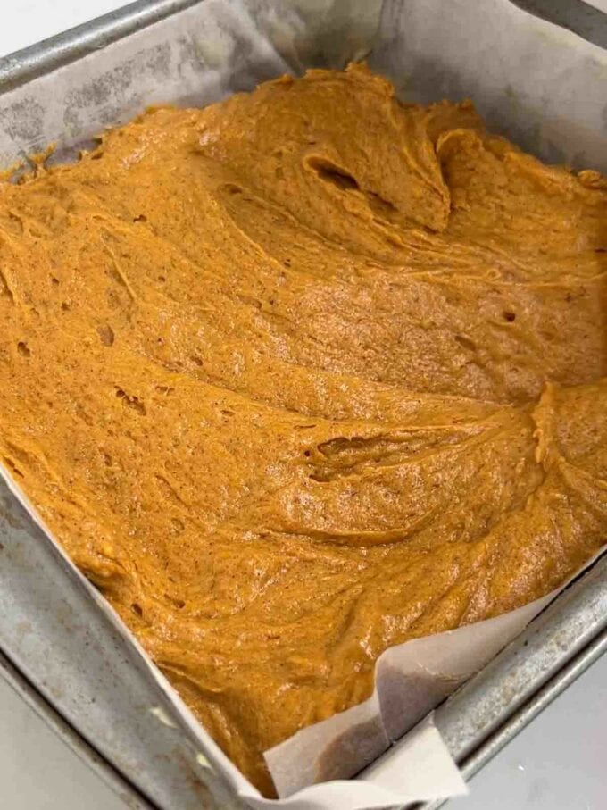 Raw pumpkin cake mixture in a lined square baking tin, ready to be baked.