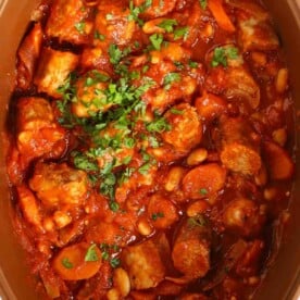 A close up image of a slow cooker casserole, with chopped sausages, carrots and beans in a tomato sauce.