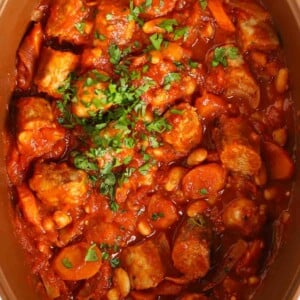 A close up image of a slow cooker casserole, with chopped sausages, carrots and beans in a tomato sauce.