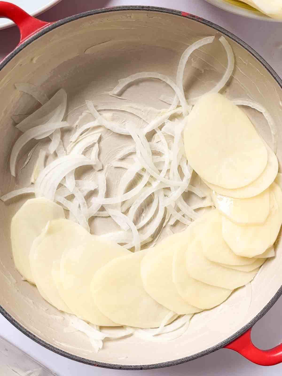 Onions in the bottom of a heavy pan with slices of potato for step 2 in the recipe for Boulangere Potatoes.