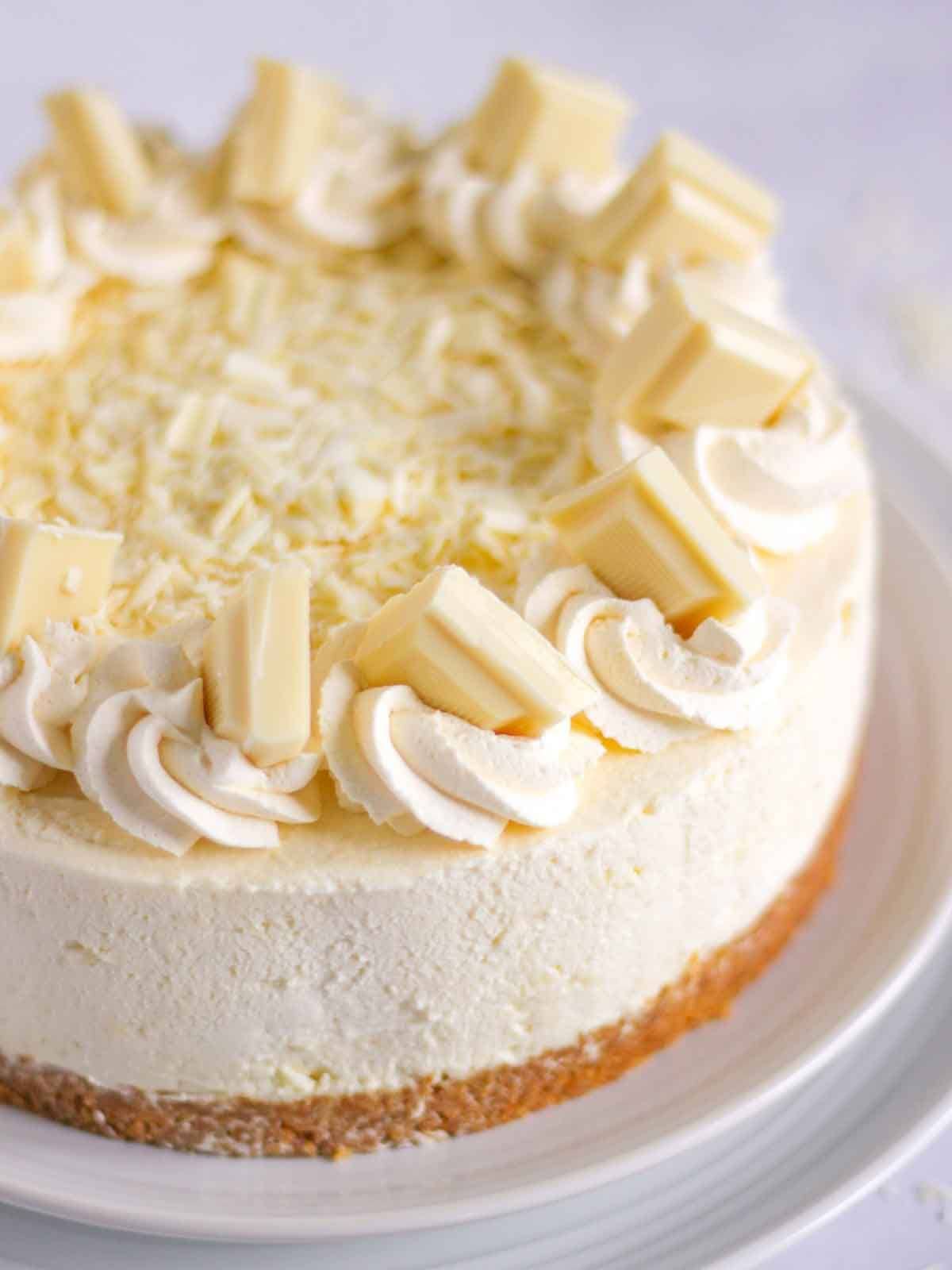 A white chocolate cheesecake on a plate with creamy swirls and white choc chunks on top.