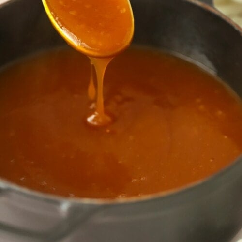 A spoon above a pan, both filled with vegetarian gravy.