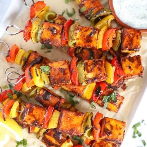A tray with cooked paneer tikka skewers on and a bowl of raita to the side.