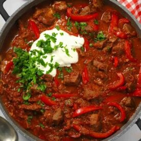 Close up of a pan filled with slow cooked beef goulash with a dollop of creme fraiche on top.