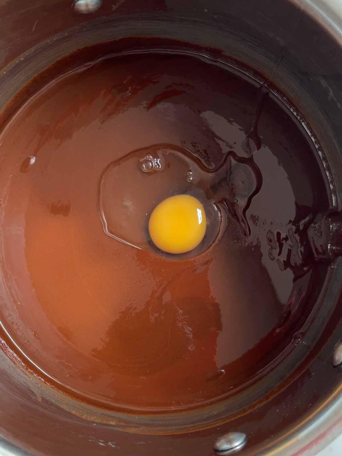 A pan filled with melted chocolate with an egg on top for step 2 in the recipe for Chocolate Orange Brownies.