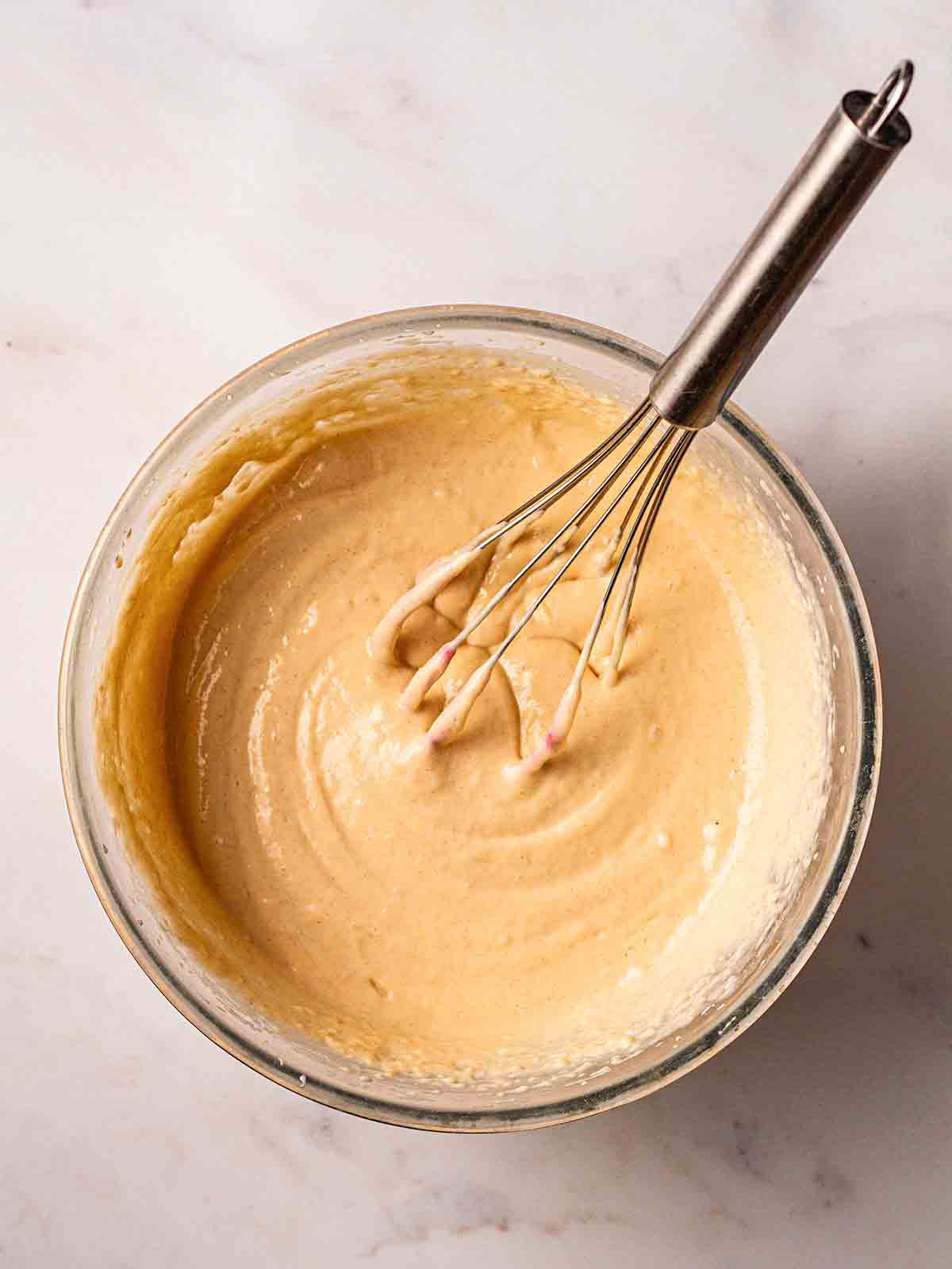 A thick batter in a jug with a whisk for step 3 in recipe for American Pancakes.