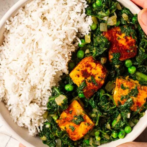 Two hands holding a bowl of cooked palak paneer and rice.