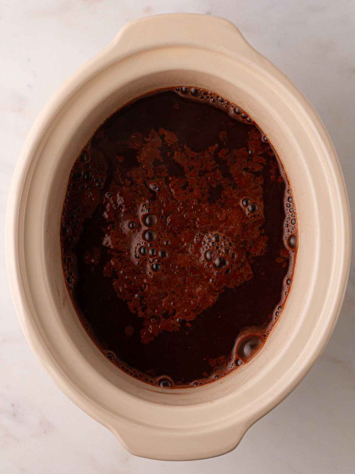 Chocolate mixture and water in a slow cooker pan for step 5 in the recipe for Slow Cooker Mini Egg Easter Pudding.