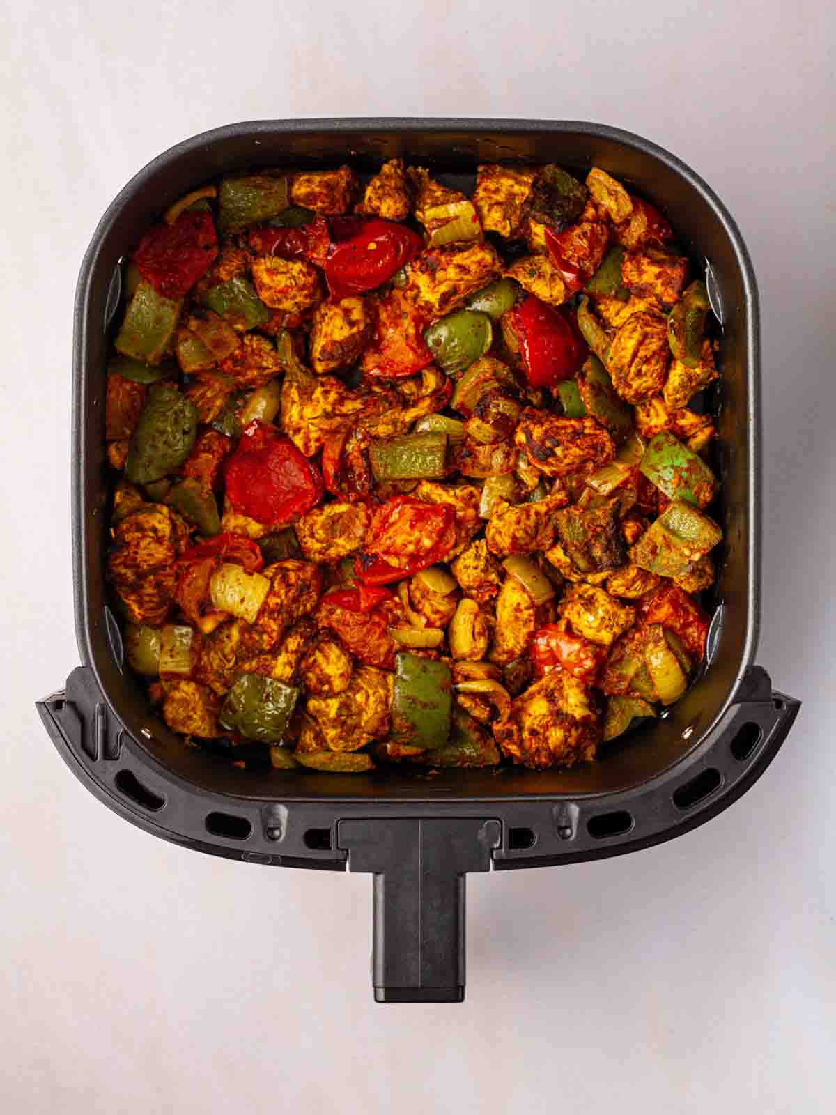 An air fryer filled with chicken pieces and vegetables for the recipe Air Fryer Chicken Tikka Tray Bake.