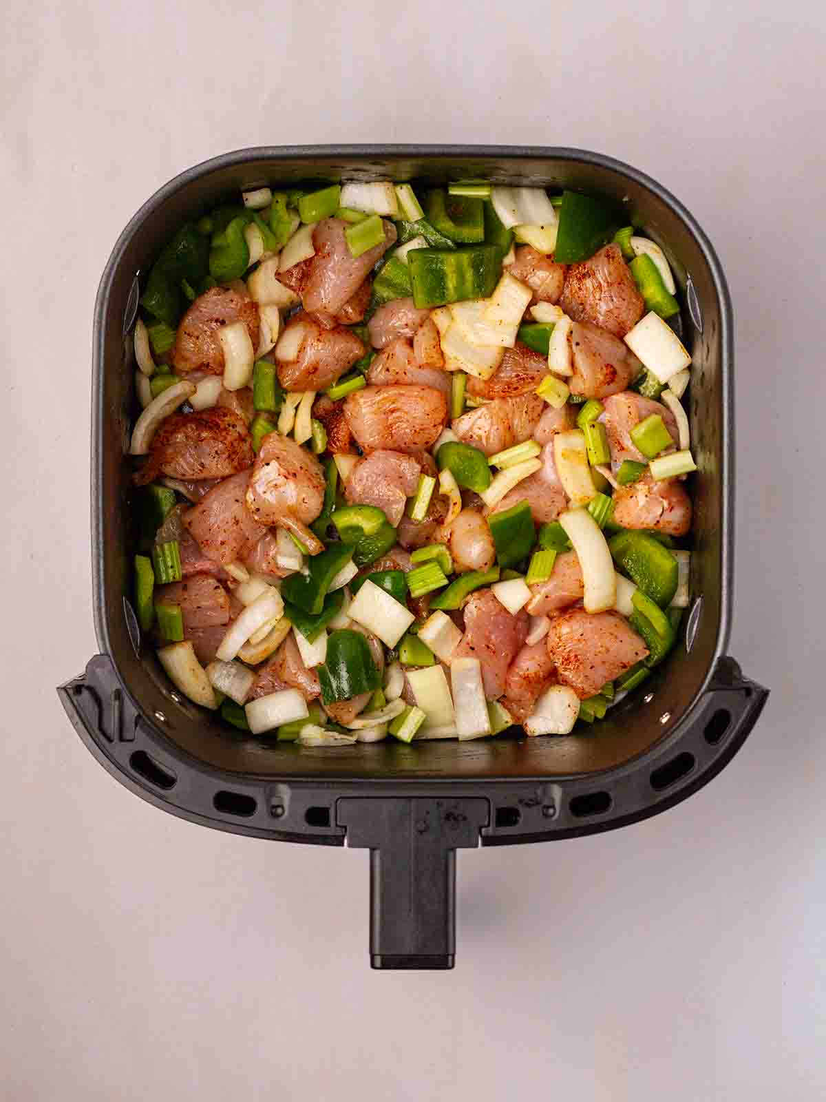 An aerial view of an air fryer with the raw ingredients inside to make air fryer cajun chicken.