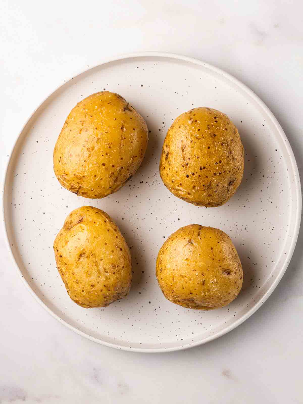 Four baked potatoes on a plate having been microwave, ready to go in the air fryer.