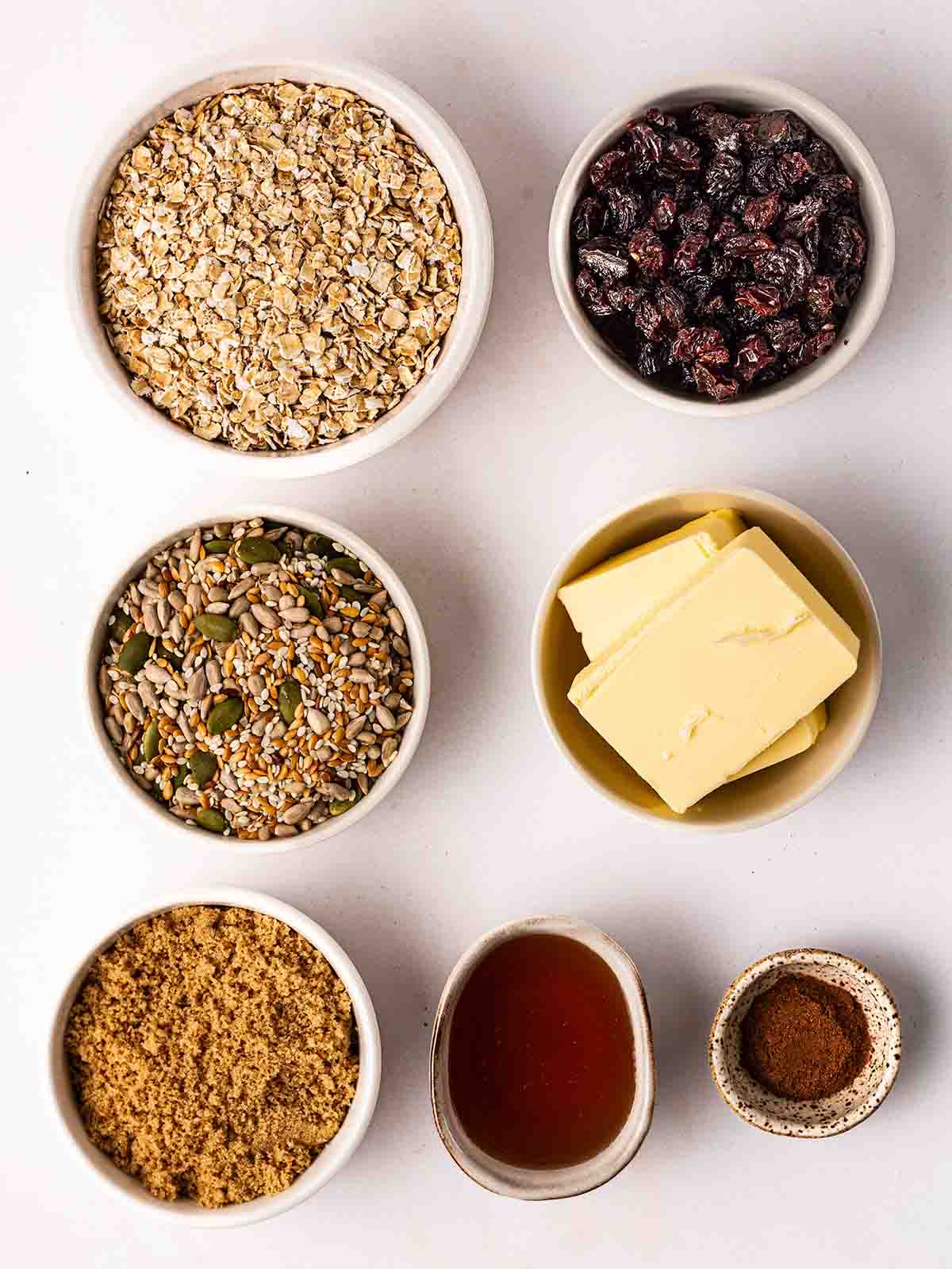 The ingredients for homemade granola bars laid out in small bowls on a white counter top.