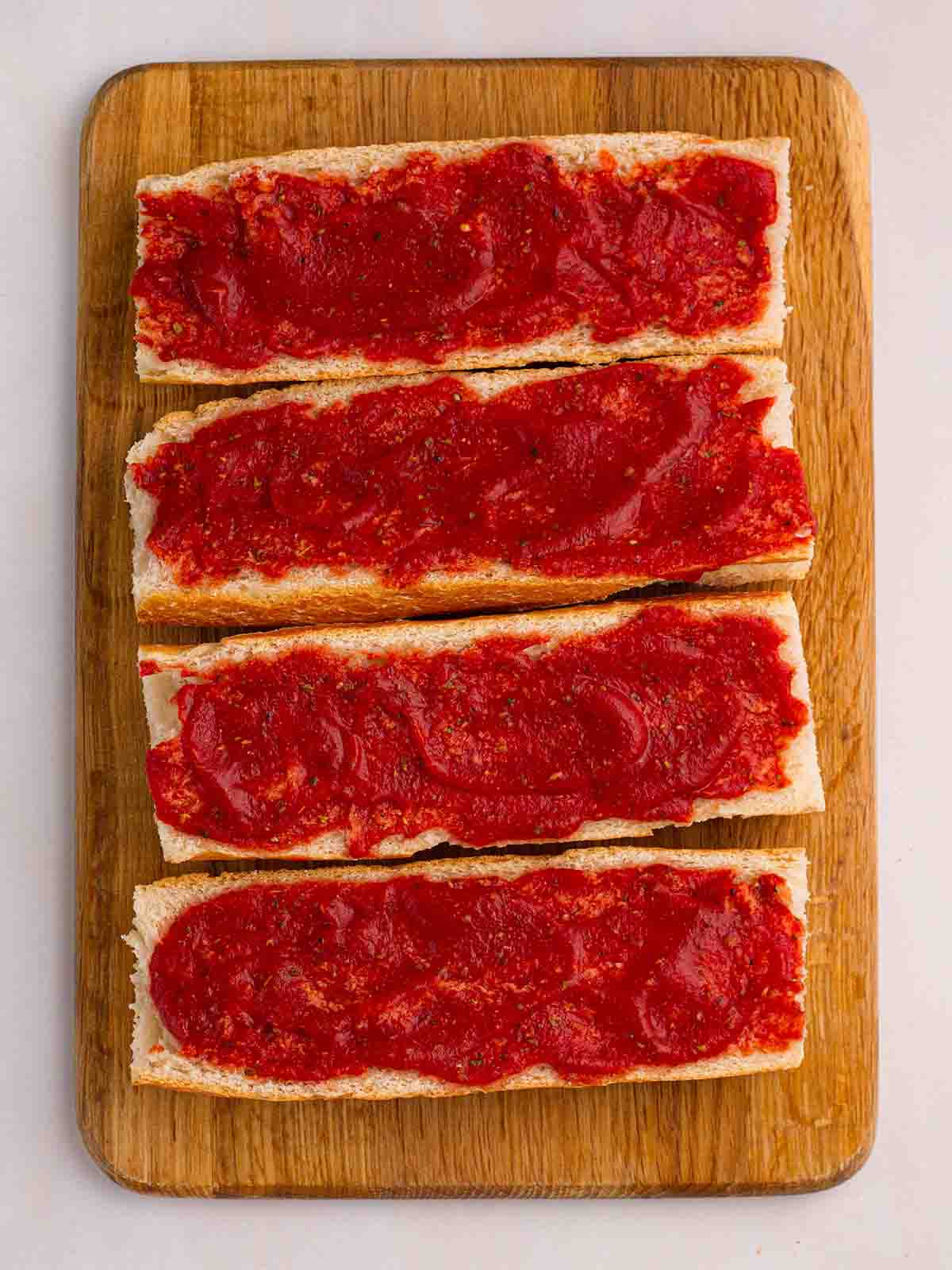 Tomato passata spread on top of halved baguettes on a chopping board.