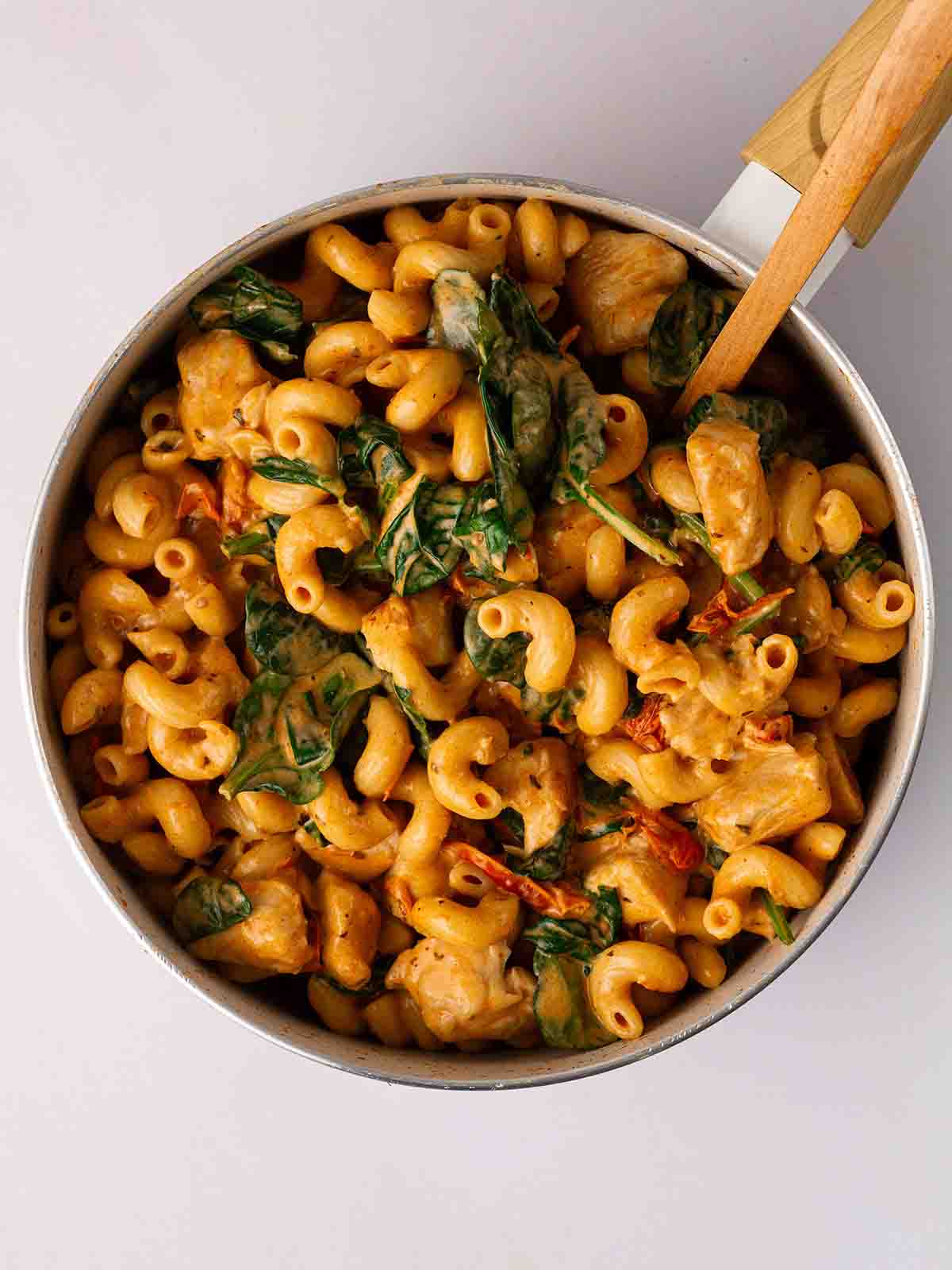 A pan filled with chicken, pasta and spinach for step 4 in the recipe for Marry Me Chicken Pasta.