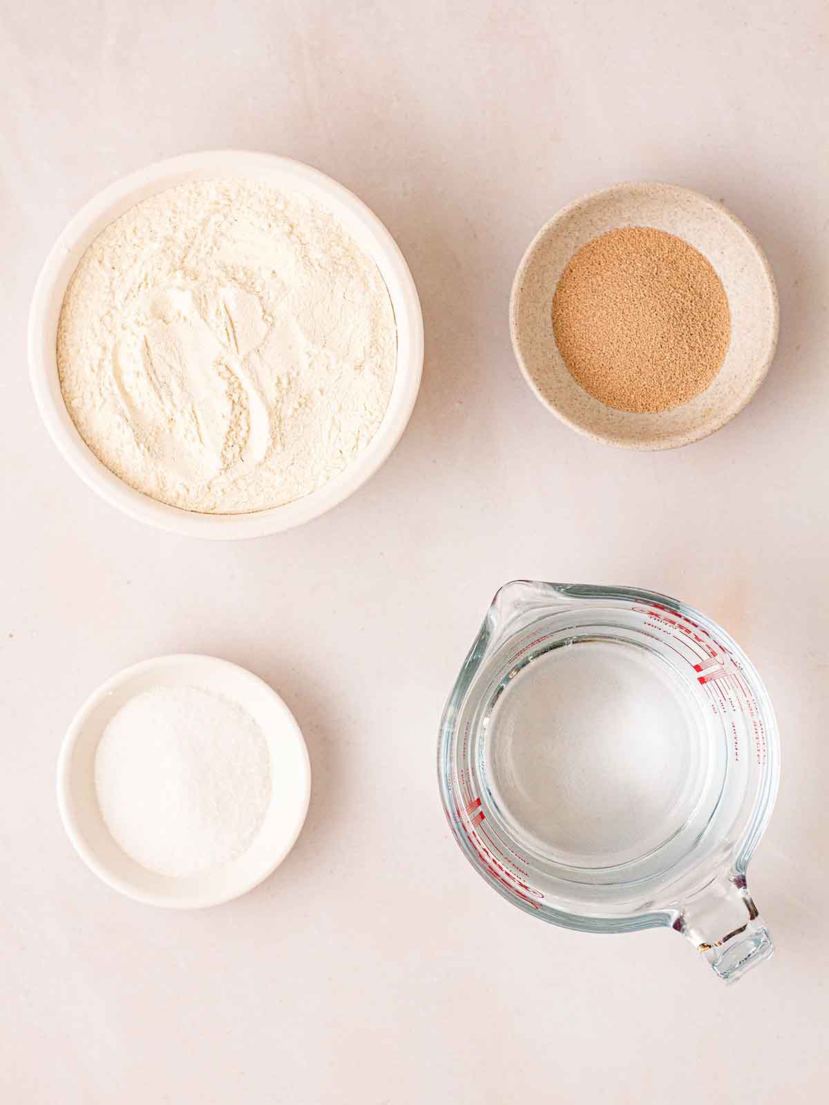 The ingredients for No Knead Bread recipe laid in bowls on a white counter.
