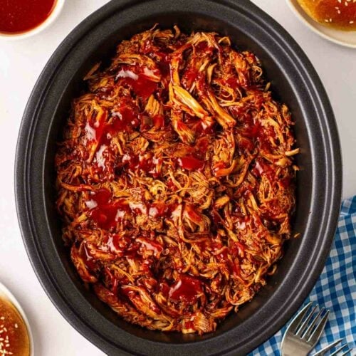 Cooked pulled pork in a slow cooker pan, ready to serve on a table with side dishes.