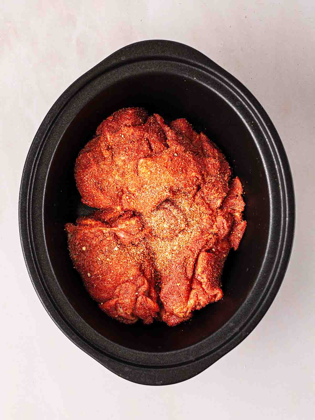 The first step of making slow cooker pulled pork, with the raw meat in the pan covered with powder ingredients.