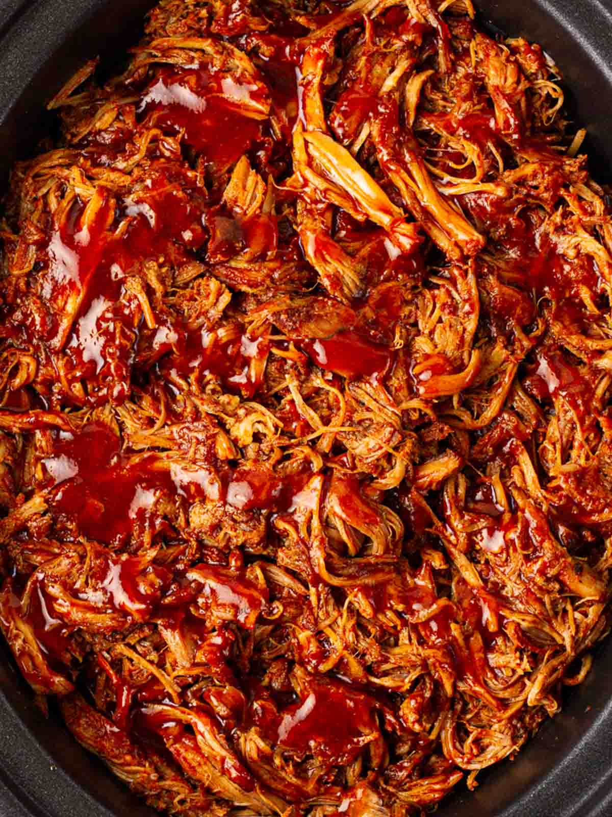 A close up of slow cooker pulled pork with red sauce on top, cooked and ready to serve.