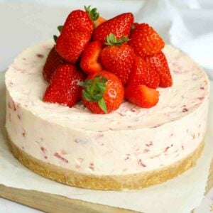 A close up of a side angle of a strawberry cheesecake, with the fruit piled high on top.