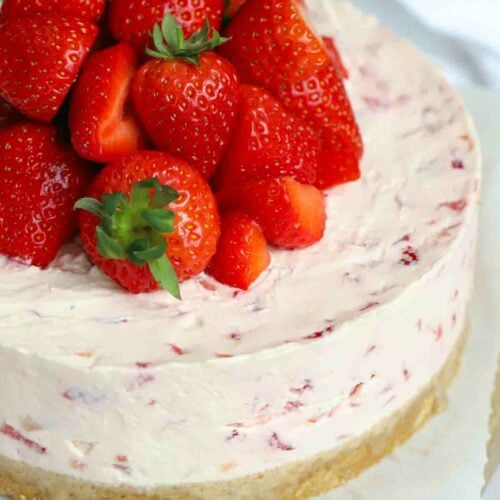 A just made Strawberry Cheesecake from the side, with a biscuit base, creamy filling and strawberries on top.