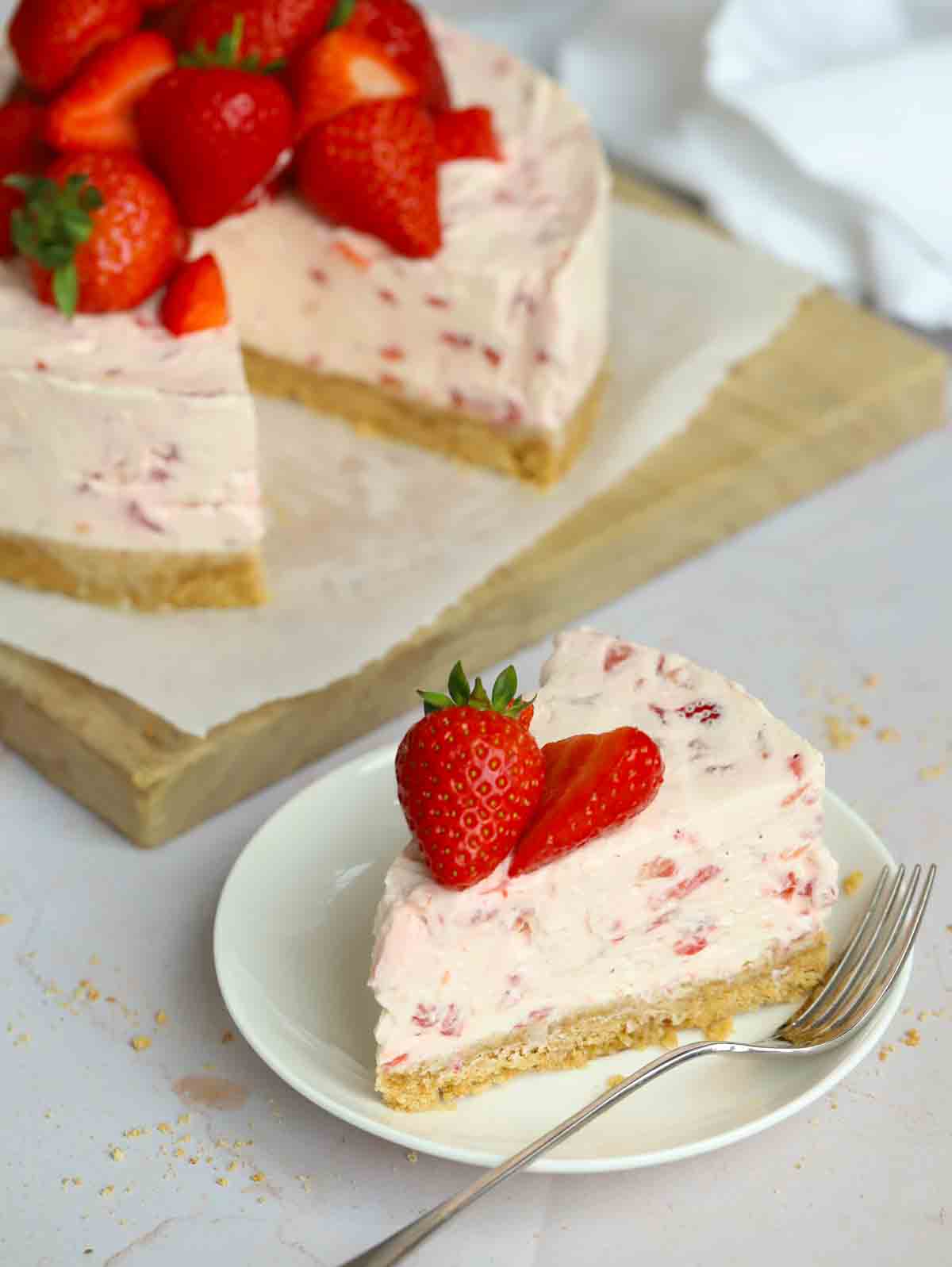 A slice of strawberry cheesecake on a side plate with a fork to the side, ready to eat.