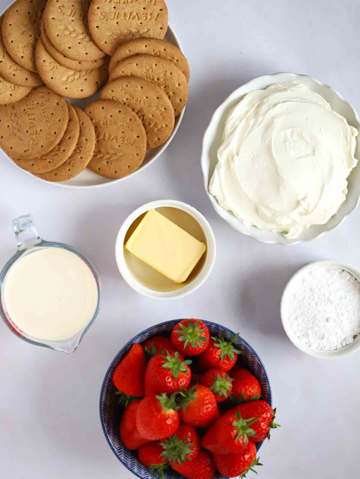 The ingredients for a strawberry cheesecake laid out in bowls on a white counter top.