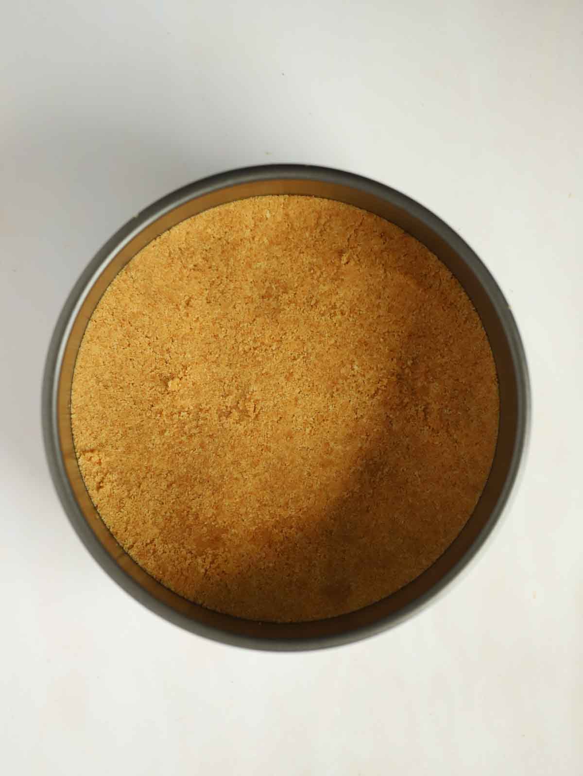 A biscuit base for a strawberry cheesecake in a tin, ready to be filled.