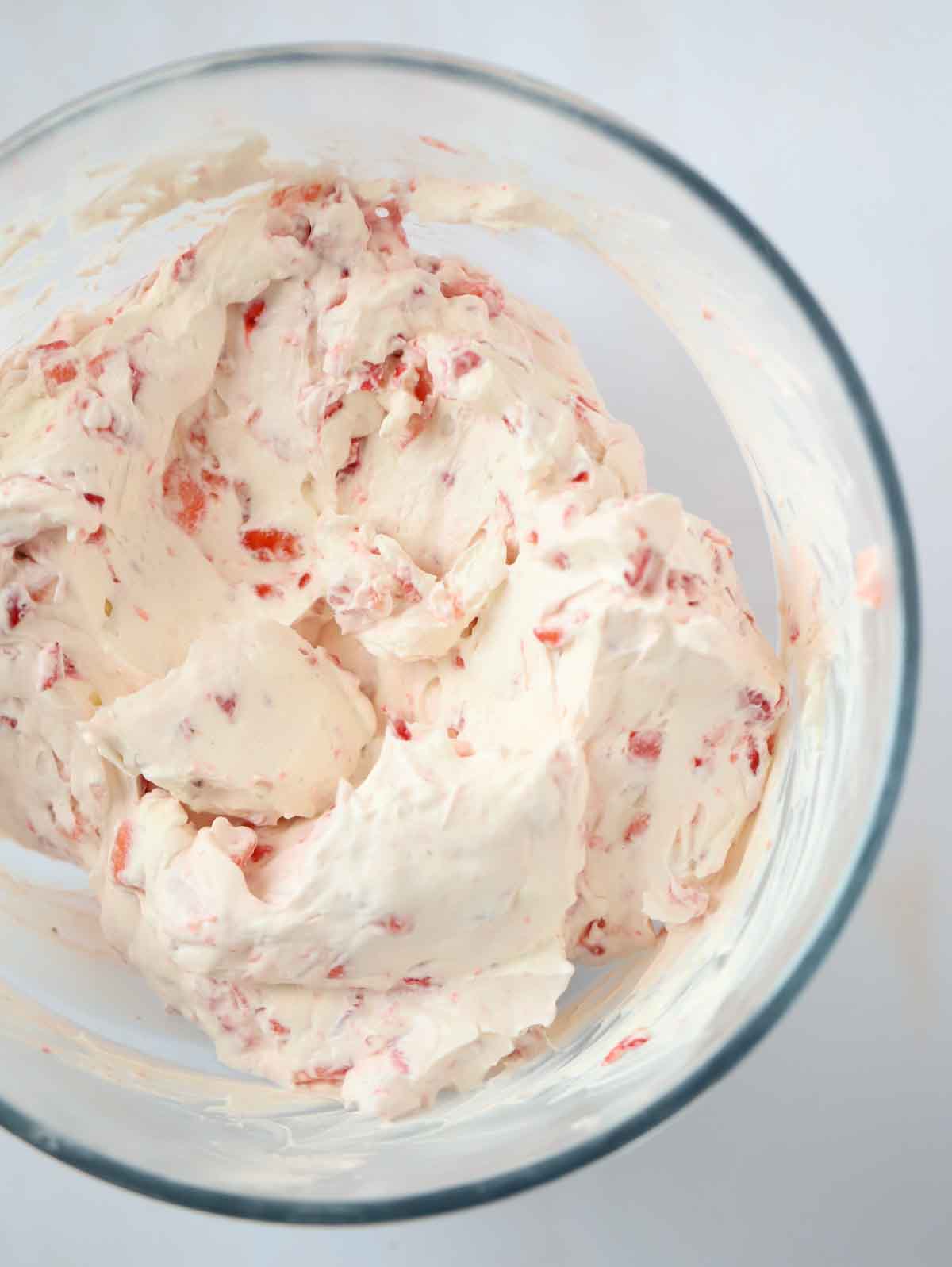 Whipped cream and cream cheese with chopped strawberries in a bowl for step 3 in the process of making a Strawberry Cheesecake.