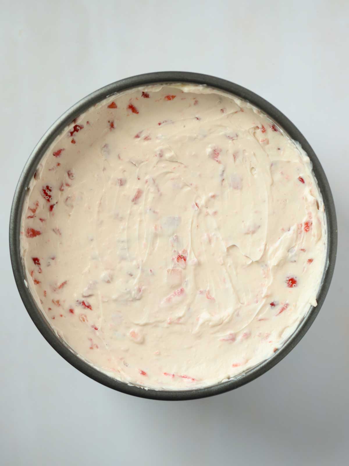 A tin filled with cream and fruit for step 4 in the recipe for strawberry cheesecake.