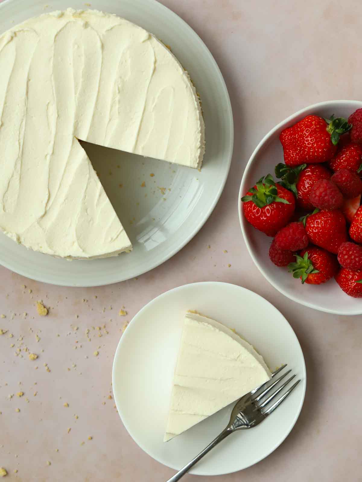 A bird's eye view of a cheesecake with a slice to the side on a plate, and a bowl of strawberries.