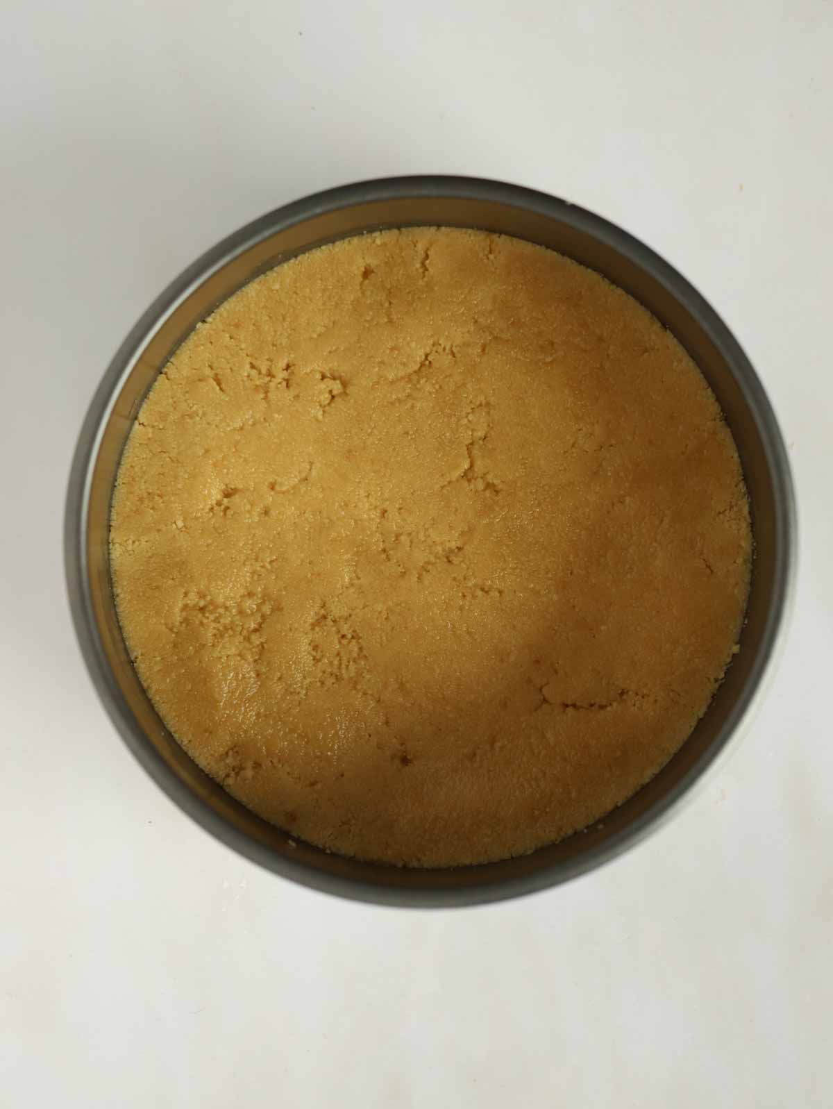 A biscuit base for a cheesecake pressed into the bottom of a tin for step 2 in the recipe for Vanilla Cheesecake.