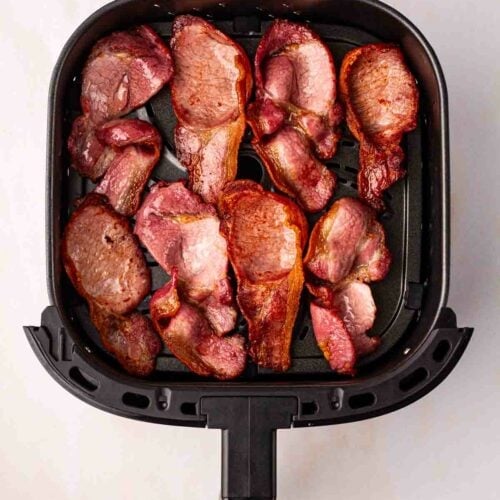An air fryer with eight rashers of cooked back bacon inside.